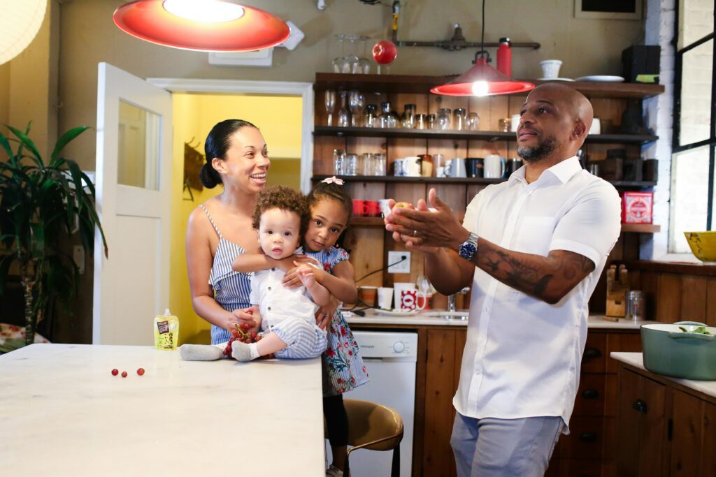 A man juggling apples in front of his family in a kitchen