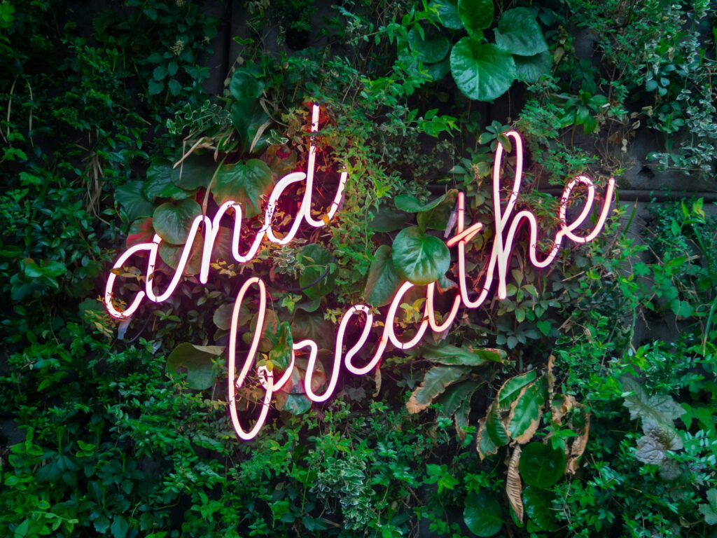 Neon sign spelling out "and breathe" on a floral background